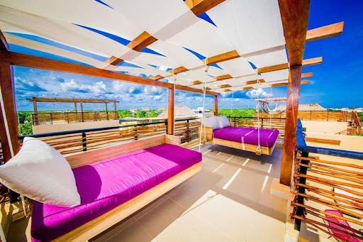 A rooftop with wood accents, a bleached linen canopy, and fuchsia hanging bed and hanging sofa in Tulum